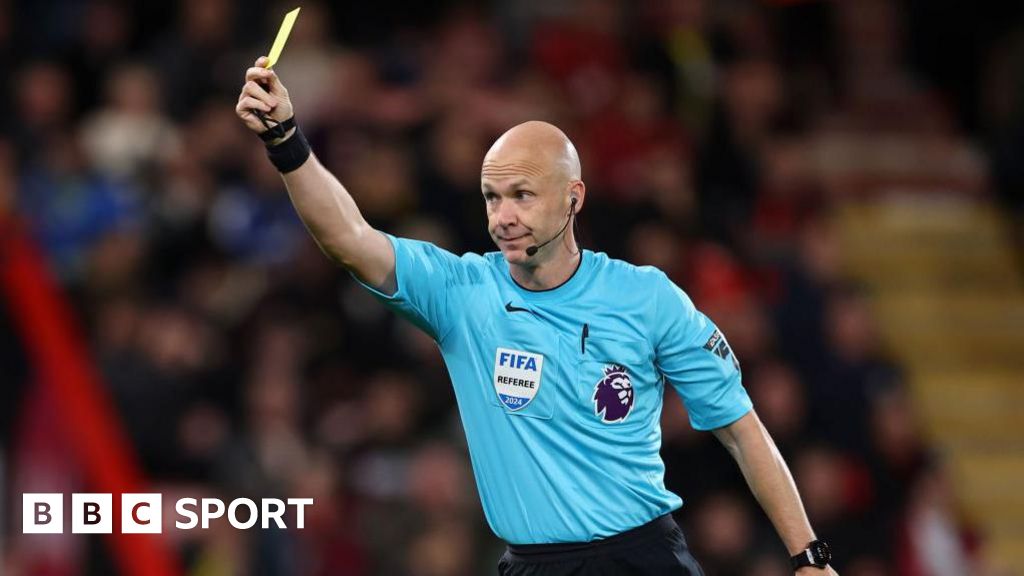 Anthony Taylor raises his arm and holds a yellow card